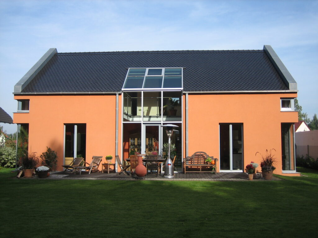 Modernes Einfamilienhaus mit orangefarbener Fassade und Glasfront, Planungsbüro.
