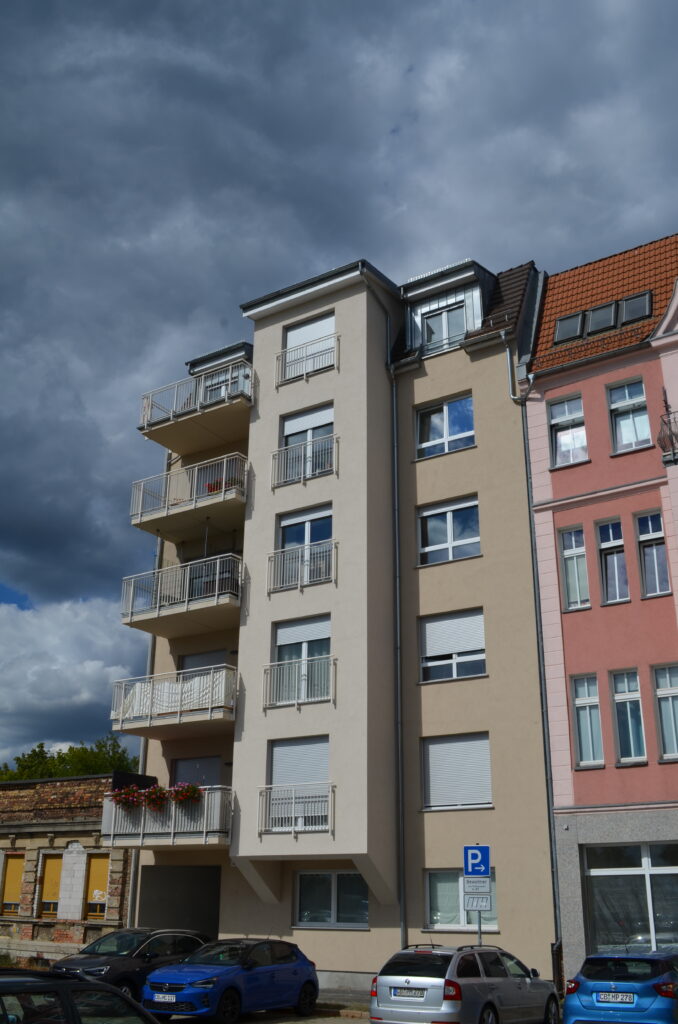 Modernes Gebäude mit Balkonen, neben einem rosafarbenen Haus, Parkplatzschild